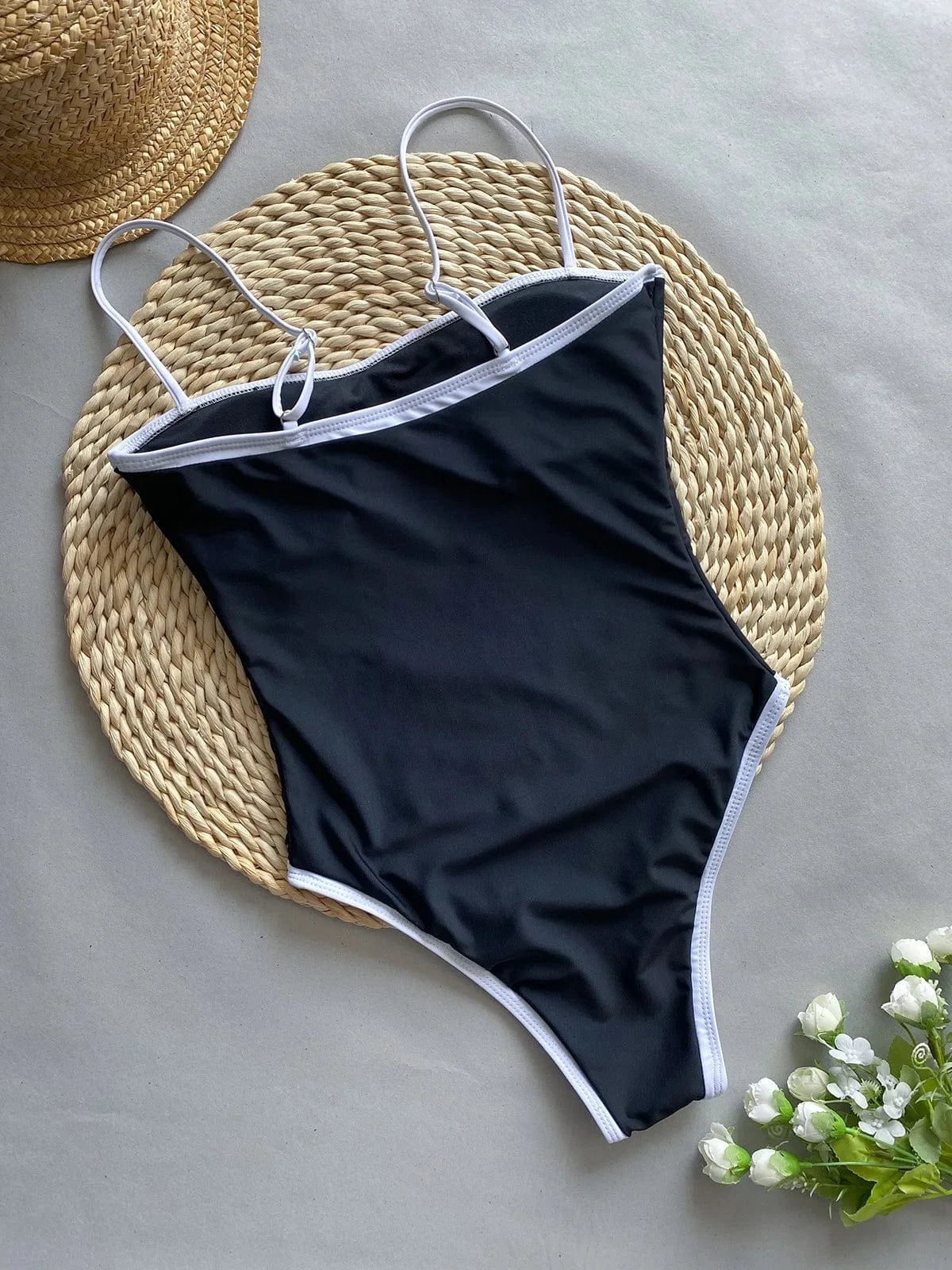 Maillot de bain une pièce noir avec bordures blanches, style échancré, posé sur un fond naturel.