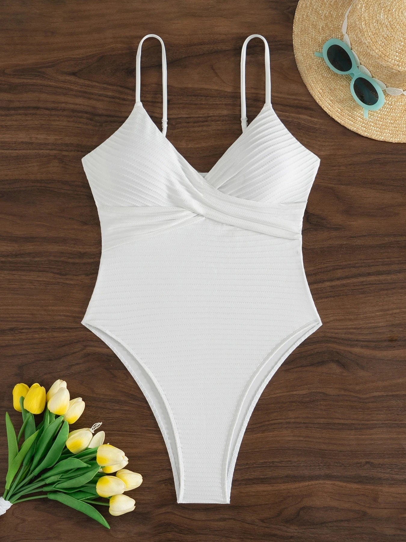 Maillot de bain une pièce blanc élégant avec bretelles fines, posé sur fond en bois sombre.