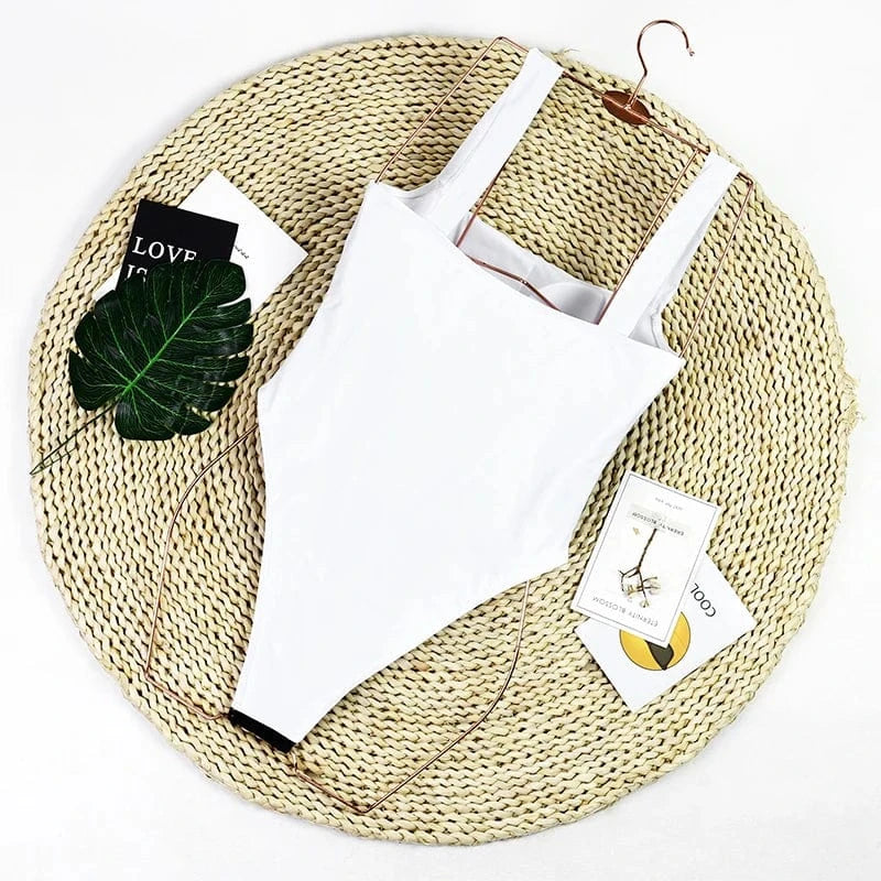 Maillot de bain une pièce blanc chic pour femme posé sur un tapis en paille avec feuille verte.