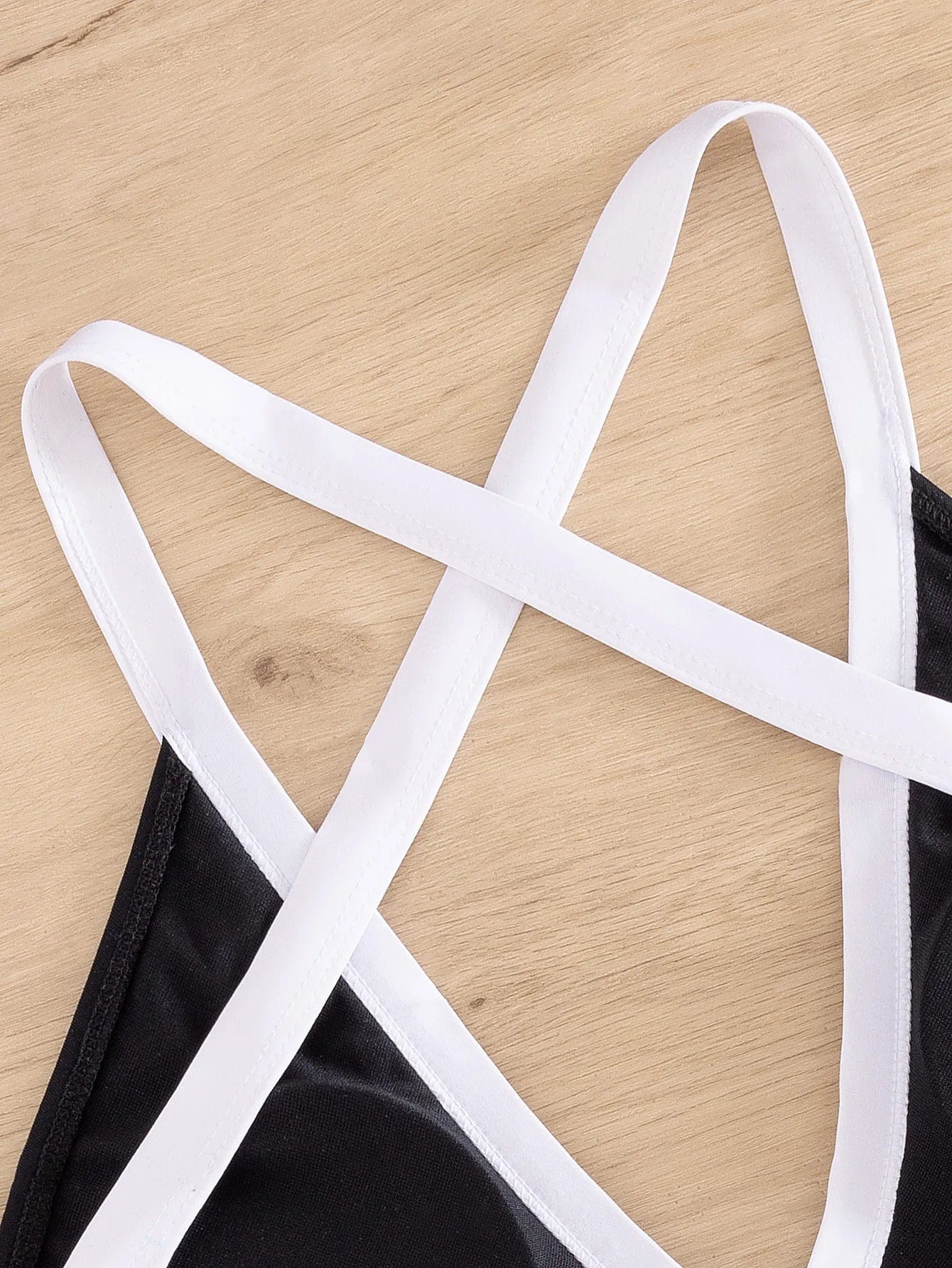 Maillot de bain une pièce noir avec bretelles croisées blanches sur fond en bois clair.