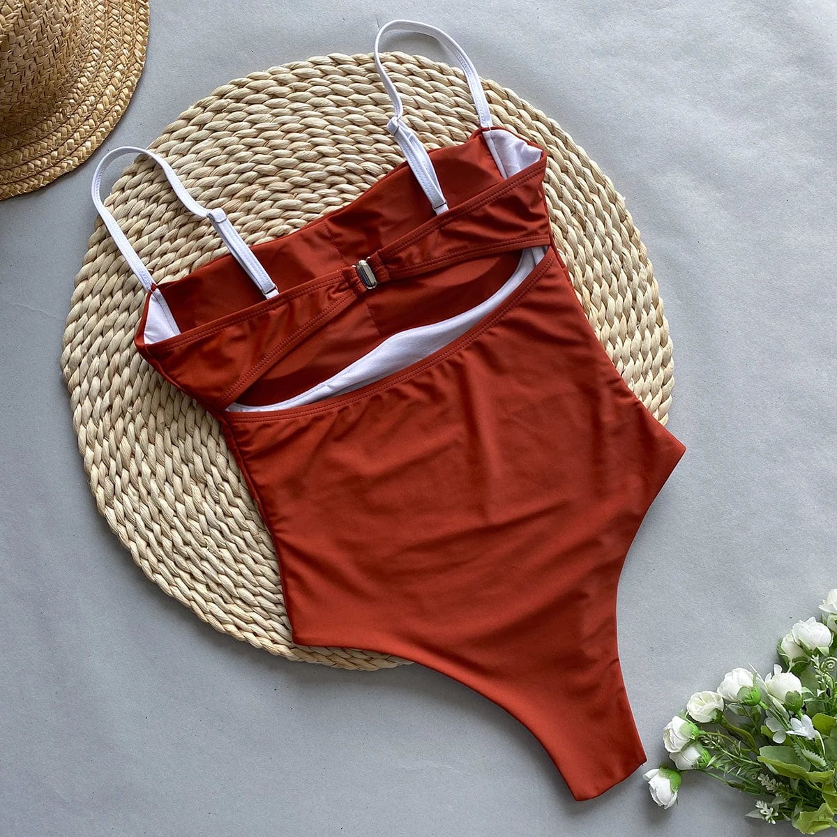 Maillot de bain une pièce marron élégant avec bretelles blanches, sur tapis tressé beige.