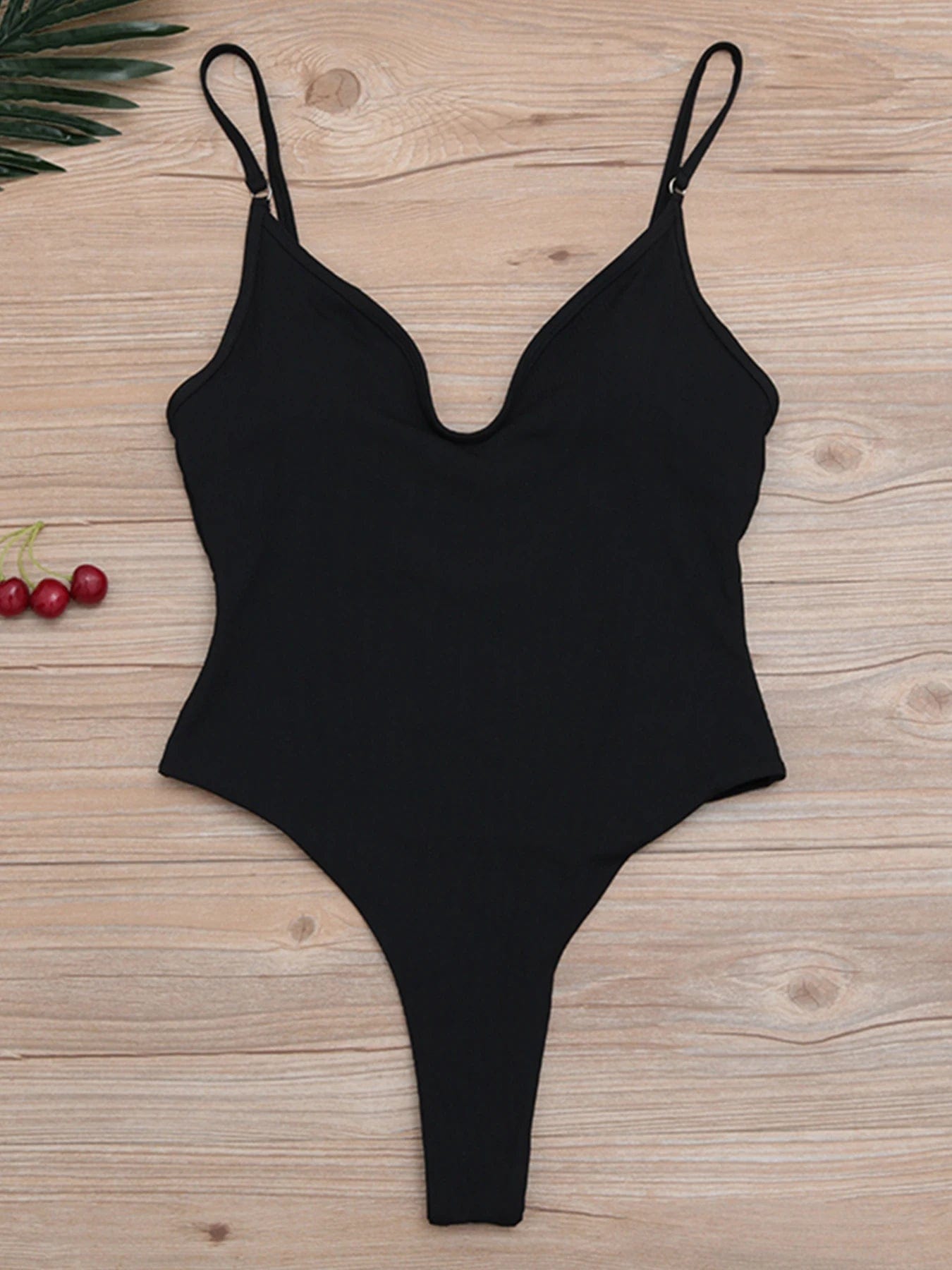 Maillot de bain une pièce noir pour femme, élégant avec bretelles fines sur fond bois clair.
