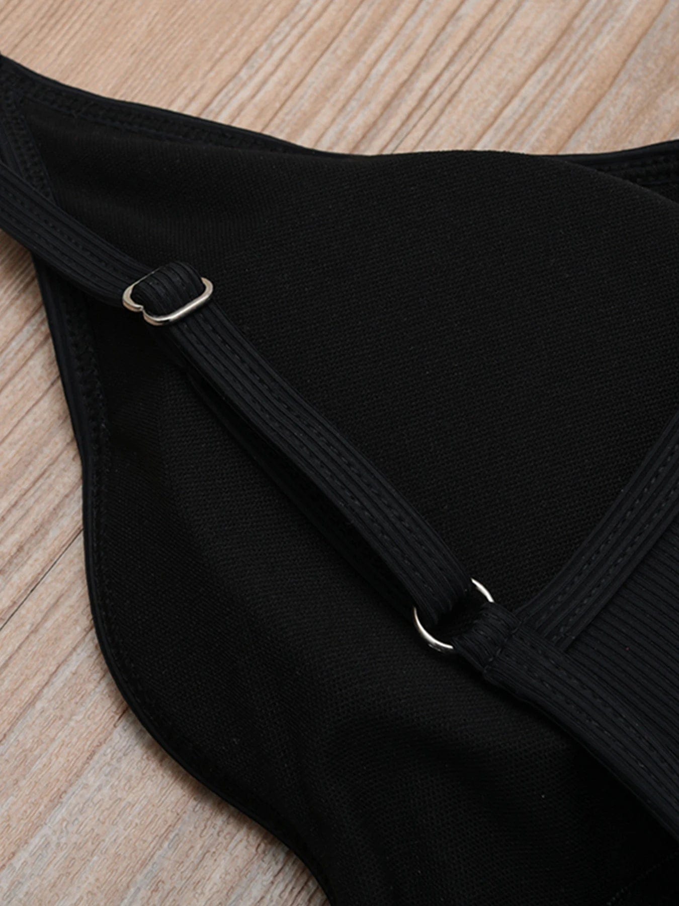 Maillot de bain une pièce noir élégant pour femme avec bretelles réglables sur fond bois.