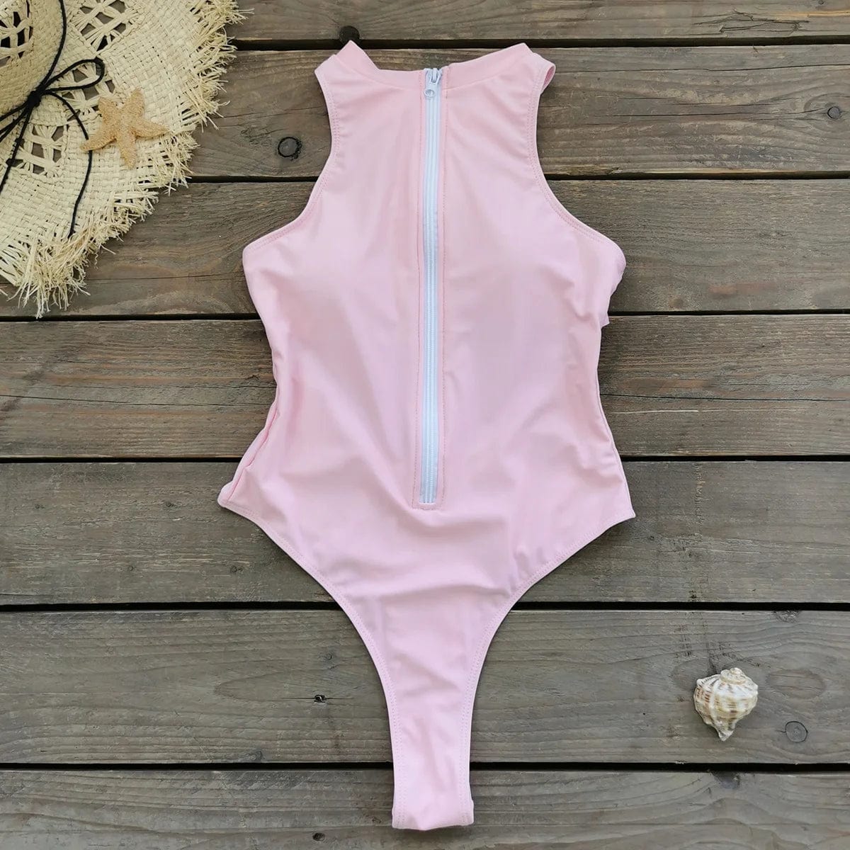 Maillot de bain une pièce rose avec fermeture éclair, posé sur fond en bois, décor estival.