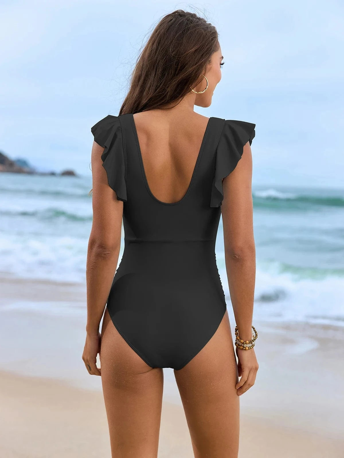 Maillot de bain élégant femme 1 pièce dos noir sur plage, aux volants, idéal pour l'été.