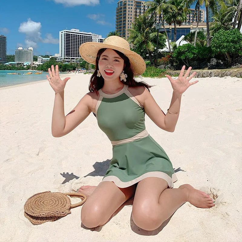 Maillot de bain une pièce vert élégant porté à la plage par une femme souriante avec un chapeau.