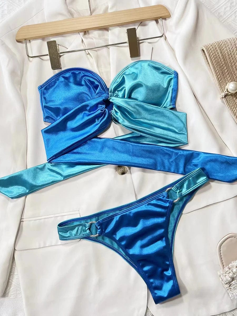 Maillot de bain bandeau femme en satin brillant bleu et turquoise sur un fond de blazer blanc.