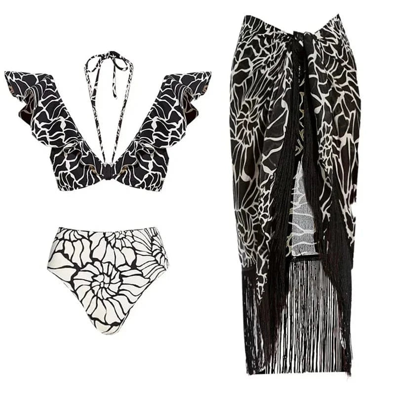 Maillot de bain femme noir et blanc avec motifs floraux et volants, accompagné d'un paréo frangé.