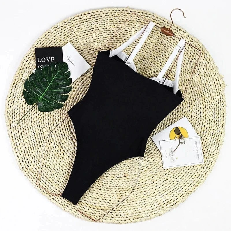 Maillot de bain une pièce noir élégant avec double bretelles, posé sur un fond estival décoratif.