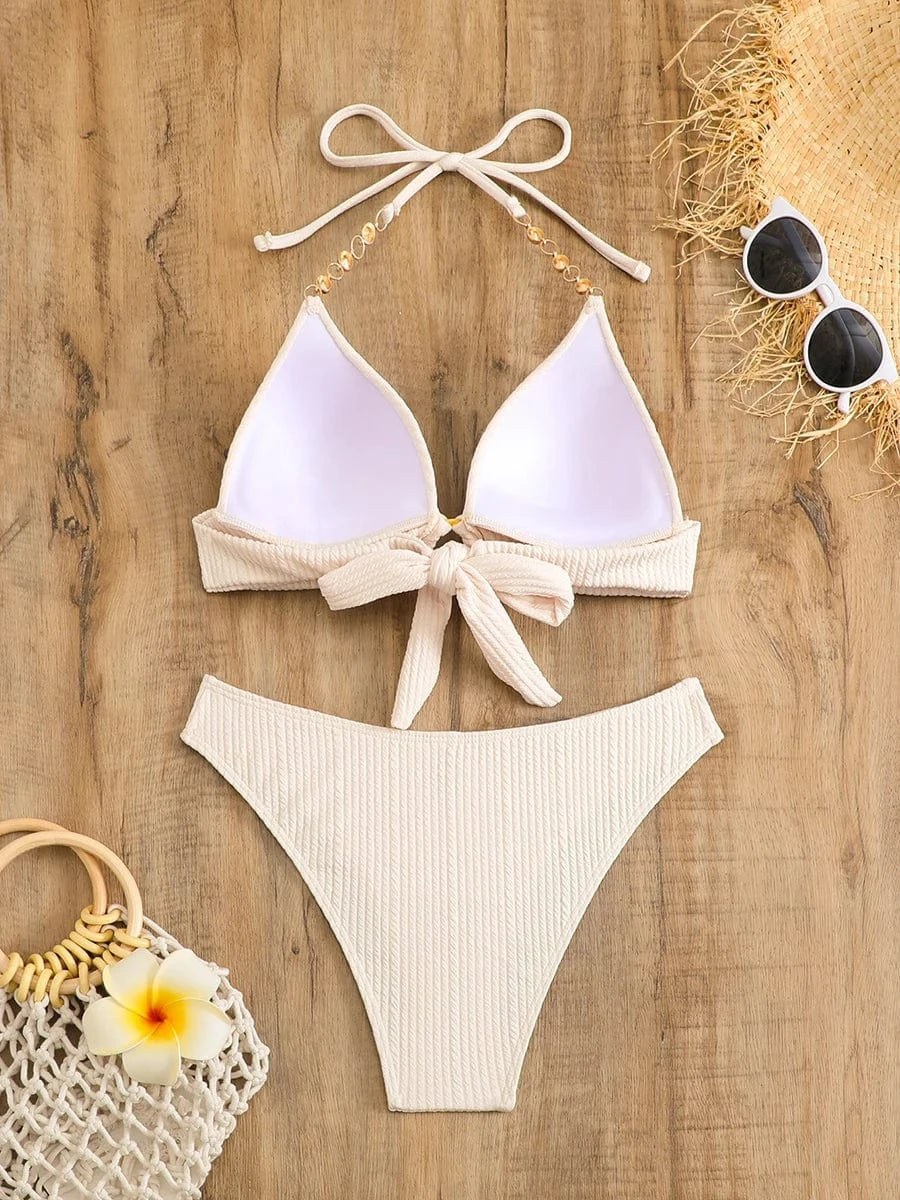 Maillot de bain femme triangle beige avec détails dorés sur fond en bois naturel et accessoires.