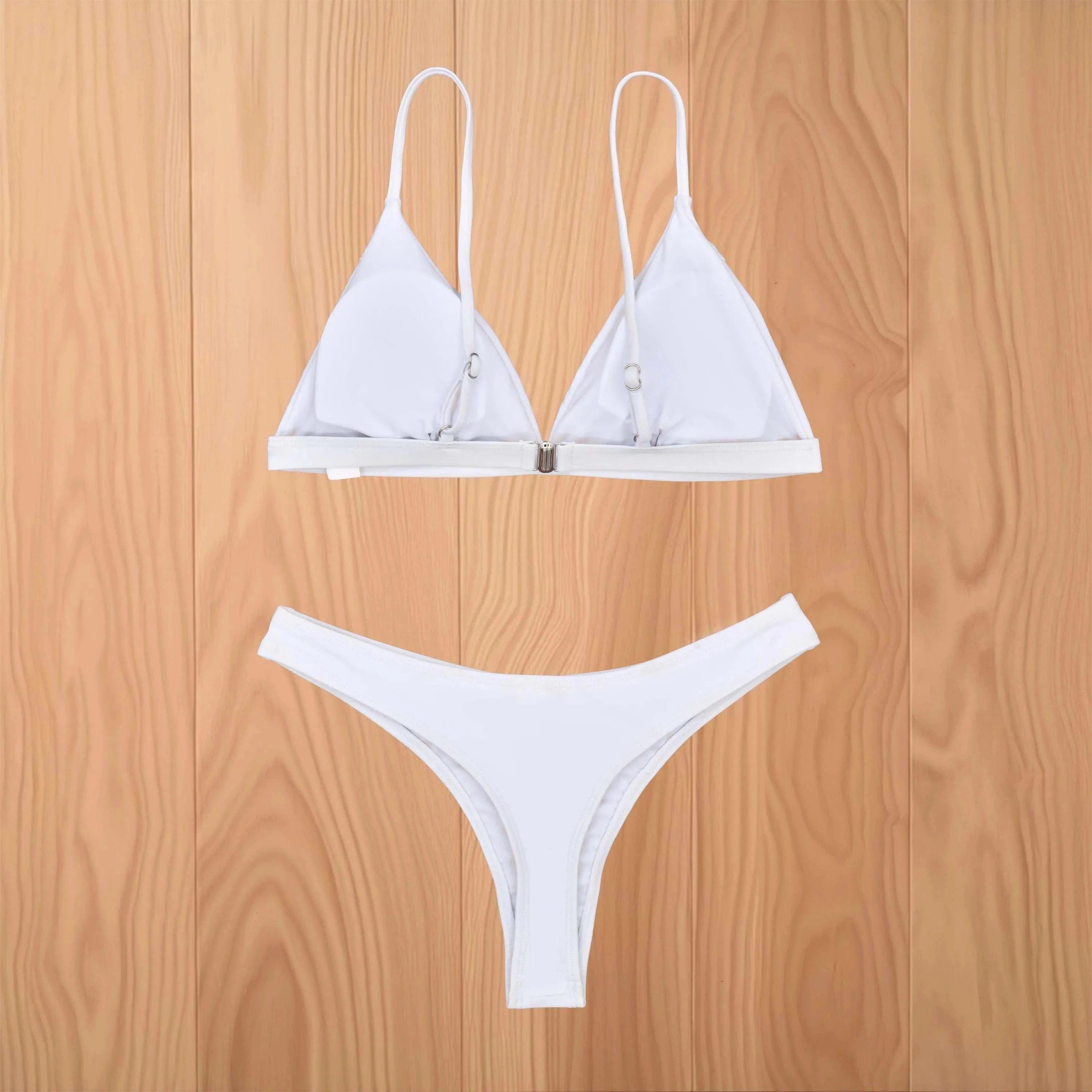 Maillot de bain triangle blanc minimaliste pour femme sur fond bois clair, style moderne et élégant.