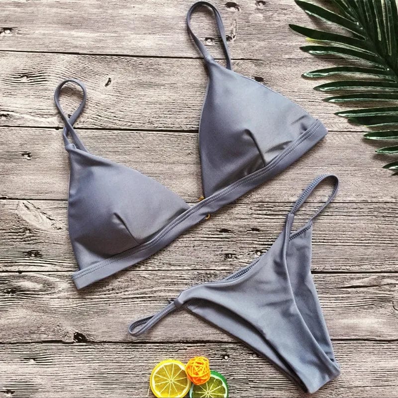 Maillot de bain femme triangle échancré gris sur fond bois avec décoration tropicale.