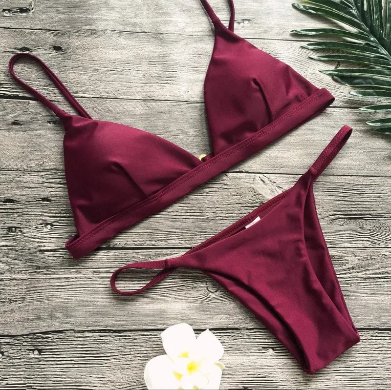 Maillot de bain femme triangle échancré bordeaux sur fond bois avec une fleur blanche.