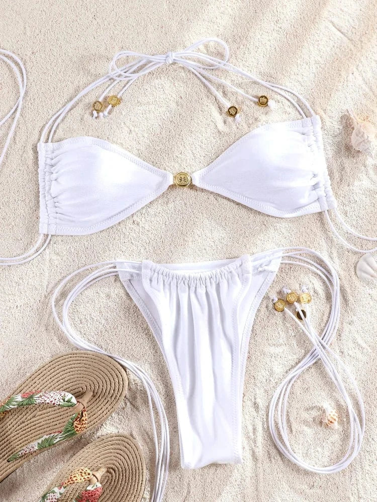 Maillot de bain femme blanc style bikini triangle avec ficelles, posé sur sable avec tongs.