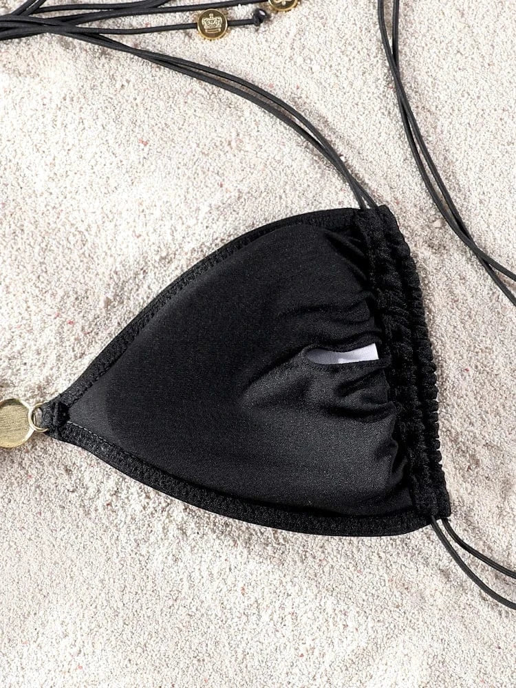 Maillot de bain noir pour femme, triangle élégant avec ficelles sur fond de sable clair.