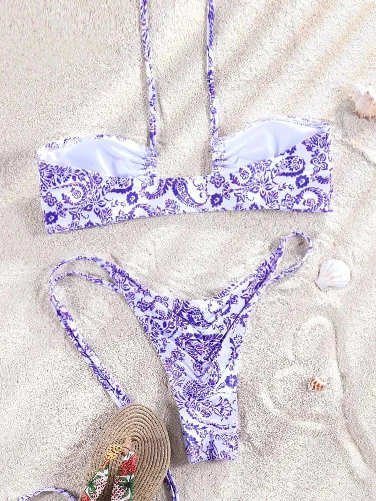 Maillot de bain bikini fleuri violet sur le sable avec coquillages et chapeau de plage.
