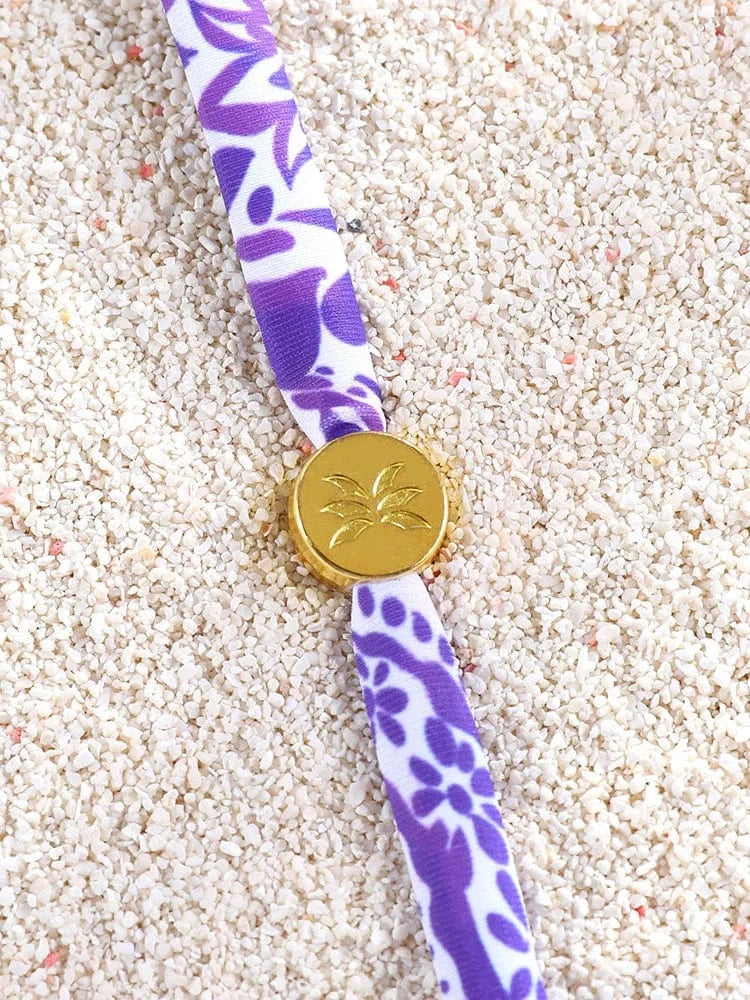 Maillot de bain femme triangle, détail de ficelle violette avec motif floral doré sur le sable.