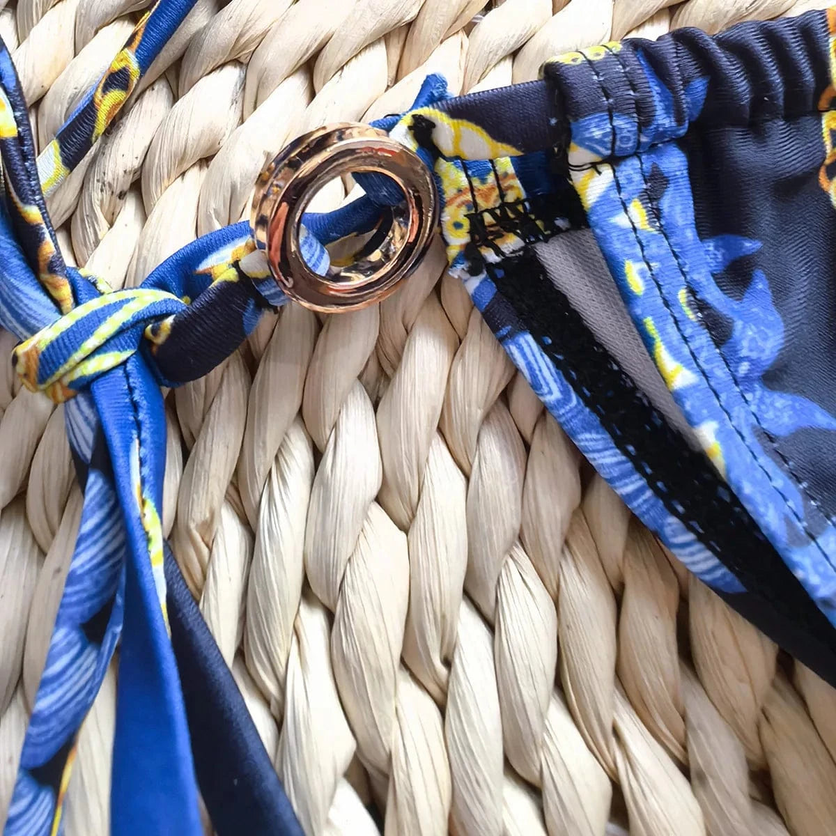 Maillot de bain femme triangle bleu avec détail doré sur fond tressé naturel élégant.