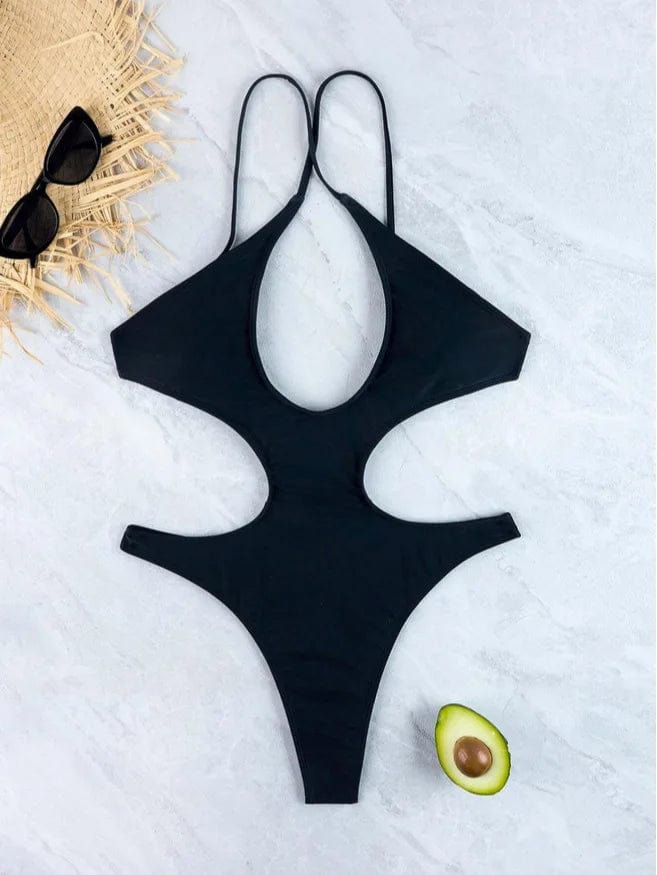 Maillot de bain une pièce noir sexy avec découpes élégantes, posé près d'un avocat et d'un chapeau.