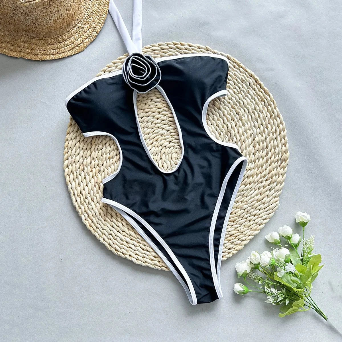 Maillot de bain une pièce noir sexy avec découpe élégante et fleurs blanches sur fond naturel.